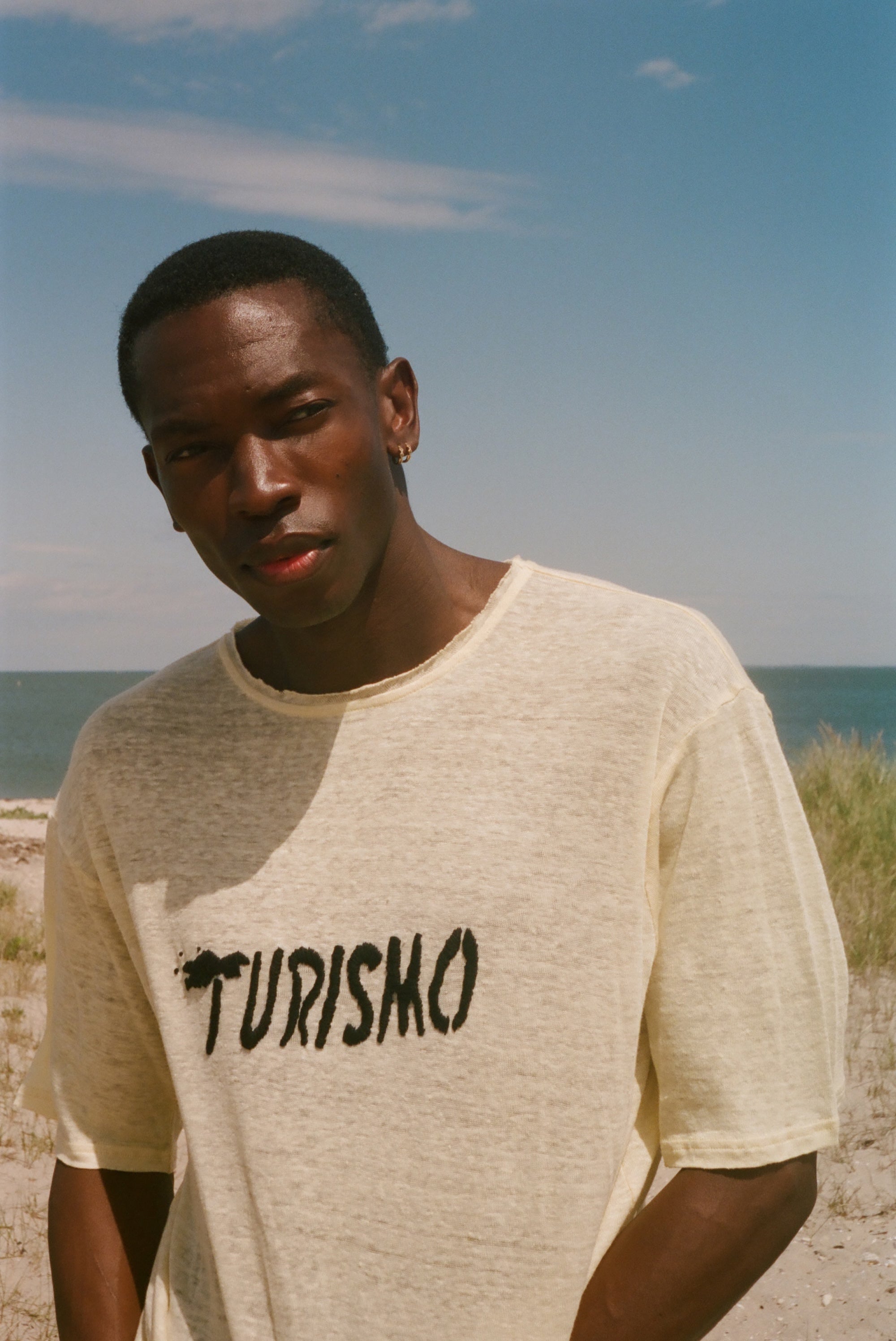 Man wearing a yellow t-shirt with 'Turismo' print on a beach