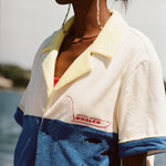 Female model wearing white sunglasses and a 'boston whaler' no nibbles cabana with a red swimsuit underneath, shot on a background of water, a thin strip of land, and blue skies.