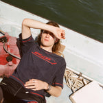Male model lying down on a boat with one hand over his head blocking the sun while he wears the 'Boston Whaler' Souvenir Terry Tee, shot on a background of the water.