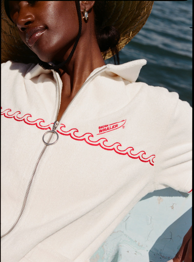 Female model wearing a large beige sunhat sitting on a boat while wearing the 'Boston Whaler' Cabana (white).