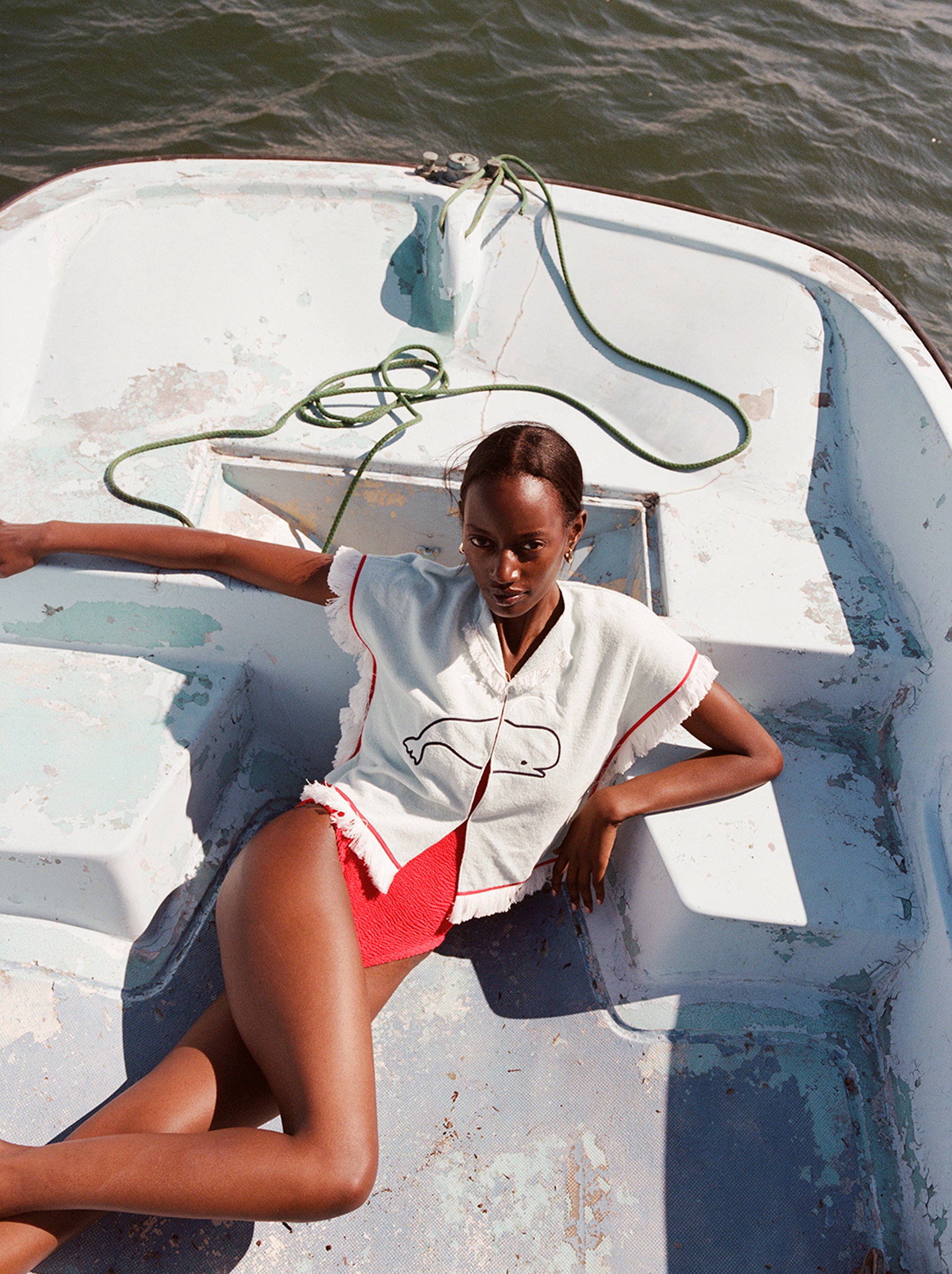 Female model on a boat lying down wearing the 'Boston Whaler' Hand Towel Top buttoned with a red bathing suit underneath.