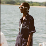 Female model with white sunglasses wearing the 'Boston Whaler' Cabana (Navy) half-zipped, standing on a boat, shot on a background of the water, a thin strip of land, and blue skies.