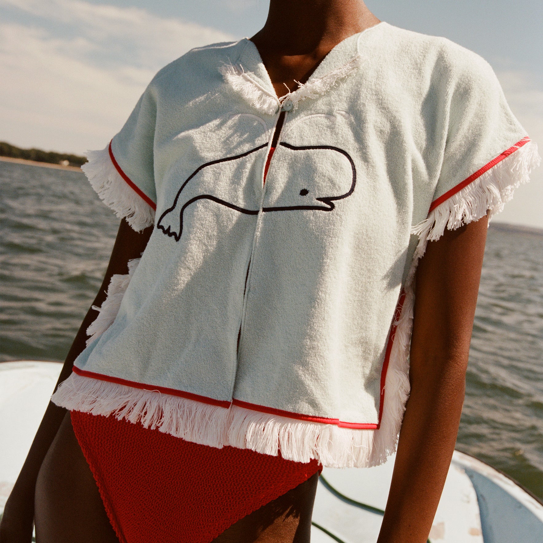 Female model wearing the 'Boston Whaler' Hand Towel Top with a red swimsuit while standing on a boat on the water.