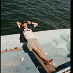 Male model wearing the 'Boston Whaler' Cabana (navy) while lying on a boat with his head over the bow, and one arm supporting it, shot on a background of the water.