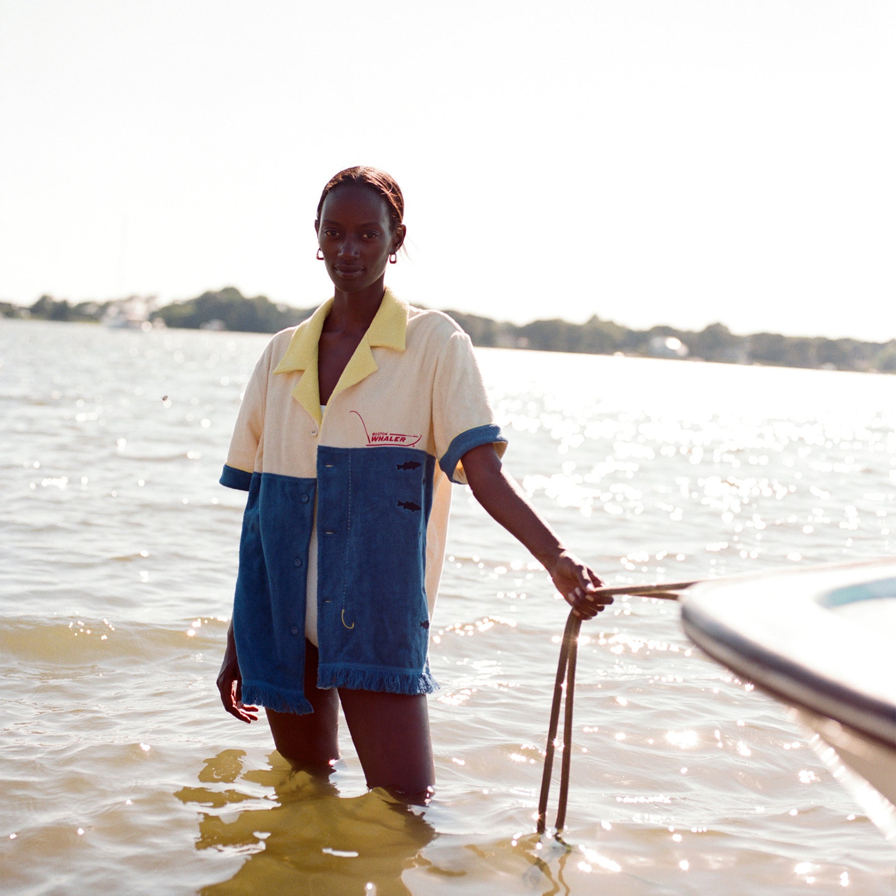 Female model holding a rope attached to a boat while standing in knee-high water wearing the 'boston whaler' no nibbles cabana.