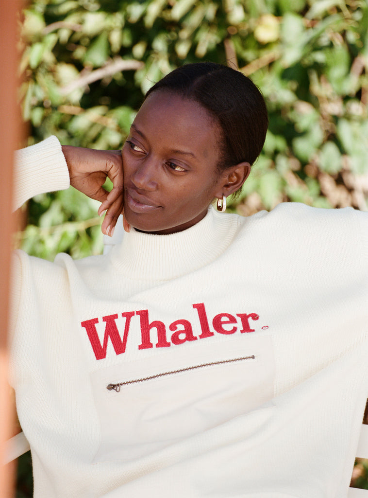 Female model with black hair wearing the 'Boston Whaler' Sweater, shot on a leafy green background.