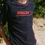 Male model with shoulder length brown hair turned to the side wearing the 'Boston Whaler' Souvenir Terry tee, shot on a background of the beach and foliage.