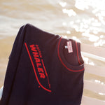 Picture of the 'boston whaler' souvenir terry tee hanging off of a white bench, shot on a background of glistening water.