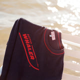 Picture of the 'boston whaler' souvenir terry tee hanging off of a white bench, shot on a background of glistening water.