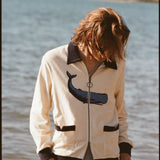 Man with long blonde hair looking down in front of water, wearing the long sleeve 'Blubber' Cabana.