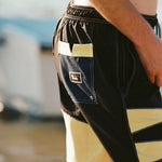 Male model wearing the 'Boston Whaler' Swim trunks while facing away from the camera to showcase the Tombolo patch on the back pocket that also has the signature Tombolo V-slit.