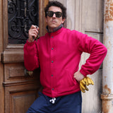 Young Male model wearing Lesca Lunetier X Tombolo Lenses alongside a bright red button up wool jacket while holding keys and leaning against a wooden door.