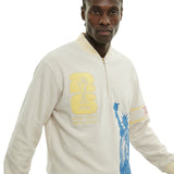 Close view of model wearing beige long sleeve terry quarter zip with FIFA World Cup New York New Jersey patch and Statue of Liberty print.