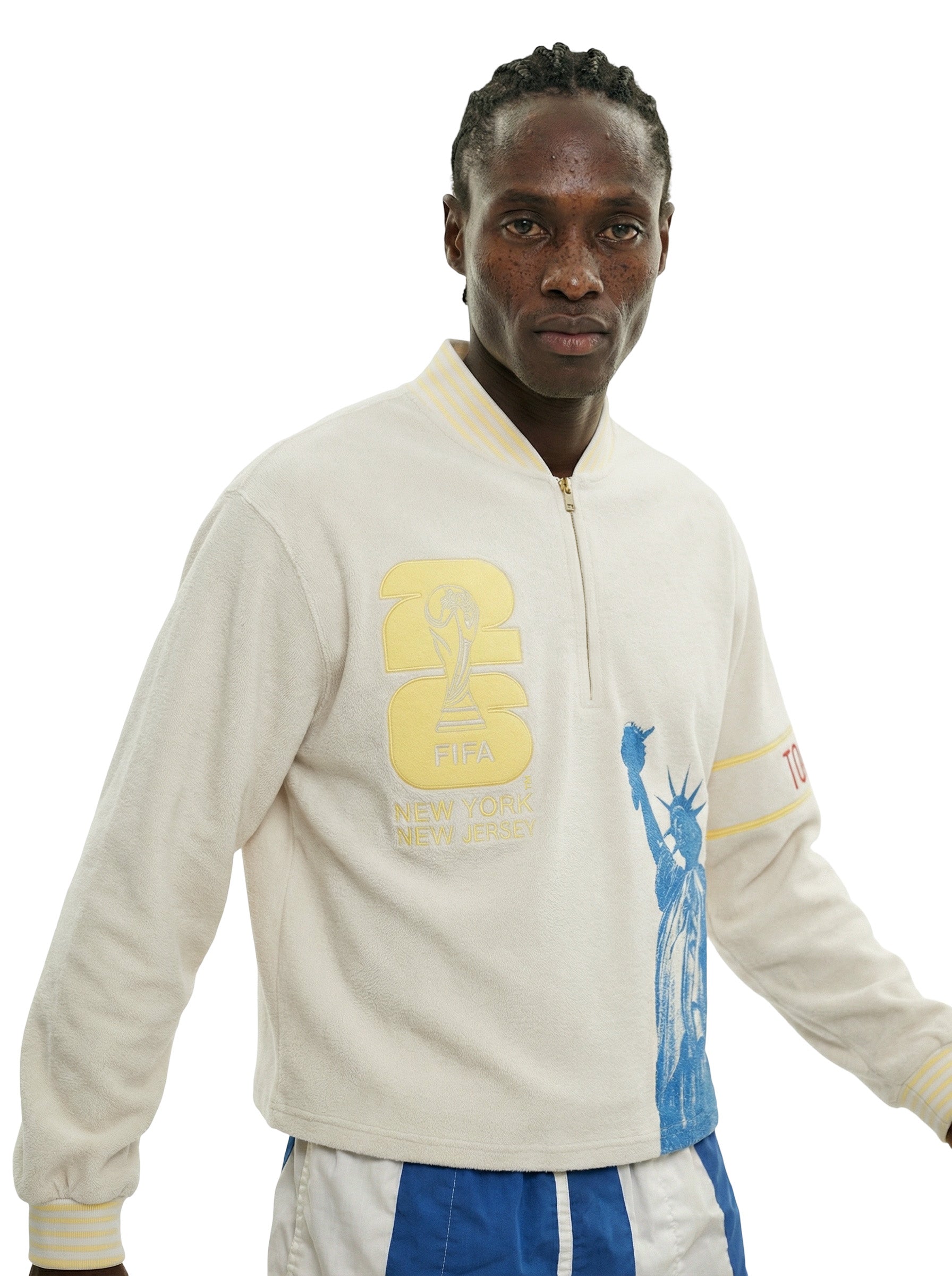 Close view of model wearing beige long sleeve terry quarter zip with FIFA World Cup New York New Jersey patch and Statue of Liberty print.