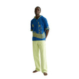 Man wearing a blue and yellow beach towel top with light green pants.