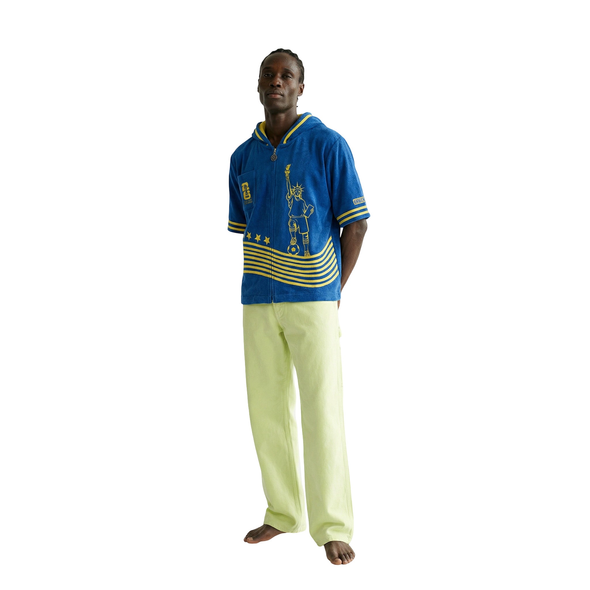 Man wearing a blue and yellow beach towel top with light green pants.