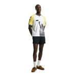 Front view of a white terry cloth shirt with yellow raglan sleeves, black sleeve lettering, a short zip neckline, and a black Statue of Liberty graphic printed on the front, worn with black striped shorts.