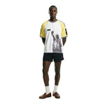 Male model wearing a white short sleeve terry cloth shirt with yellow raglan sleeves, quarter-zip neckline, and a black Statue of Liberty graphic on the front, featuring FIFA World Cup 26 branding on the chest and sleeves.