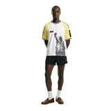 Male model wearing a white short sleeve terry cloth shirt with yellow raglan sleeves, quarter-zip neckline, and a black Statue of Liberty graphic on the front, featuring FIFA World Cup 26 branding on the chest and sleeves.