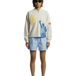 Model wearing beige long sleeve terry quarter zip with FIFA World Cup graphics and Statue of Liberty print.