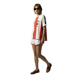 Female model wearing a white and red striped terry cloth short sleeve shirt with FIFA World Cup 26 patches on the chest and sleeve, paired with white athletic shorts.
