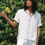 man holds leaves from background wearing linen shirt and matching oyster trunks
