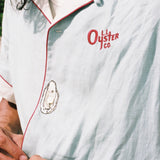 close up of man buttoning the linen oyster shirt showing the embroidered oyster motif