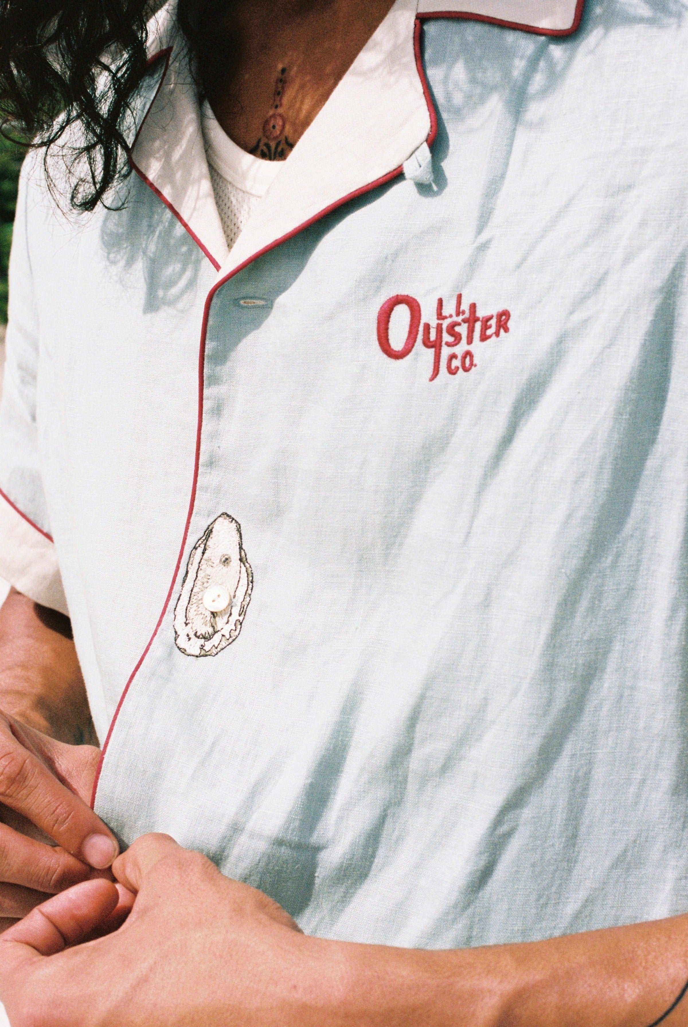 close up of man buttoning the linen oyster shirt showing the embroidered oyster motif