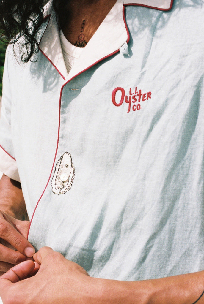 close up of man buttoning the linen oyster shirt showing the embroidered oyster motif