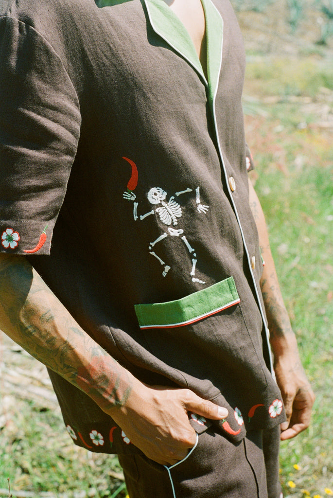 Close up view of embroidered skeleton holding a chili pepper. 