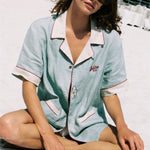 woman sits cross legged on beach wearing sunglasses and oyster shirt