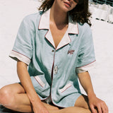 woman sits cross legged on beach wearing sunglasses and oyster shirt