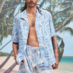 Male model with dreadlocks wearing an unbuttoned 'Palm Fronds (blue)' alongside matching 'Palm Fronds (blue) Swim Trunks,' all shot on a background with palm trees, sun, and a beach. 