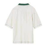 Back of a white terry cloth polo shirt with a green collar and green contrast stitching. A curved dotted line is embroidered across the upper back and sleeves, evoking the motion of a golf ball in flight.
