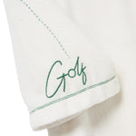 Close-up of the left sleeve of a white terry cloth polo shirt. Green embroidery reads 'Golf' in script, with a dotted line extending upward from the lettering. 