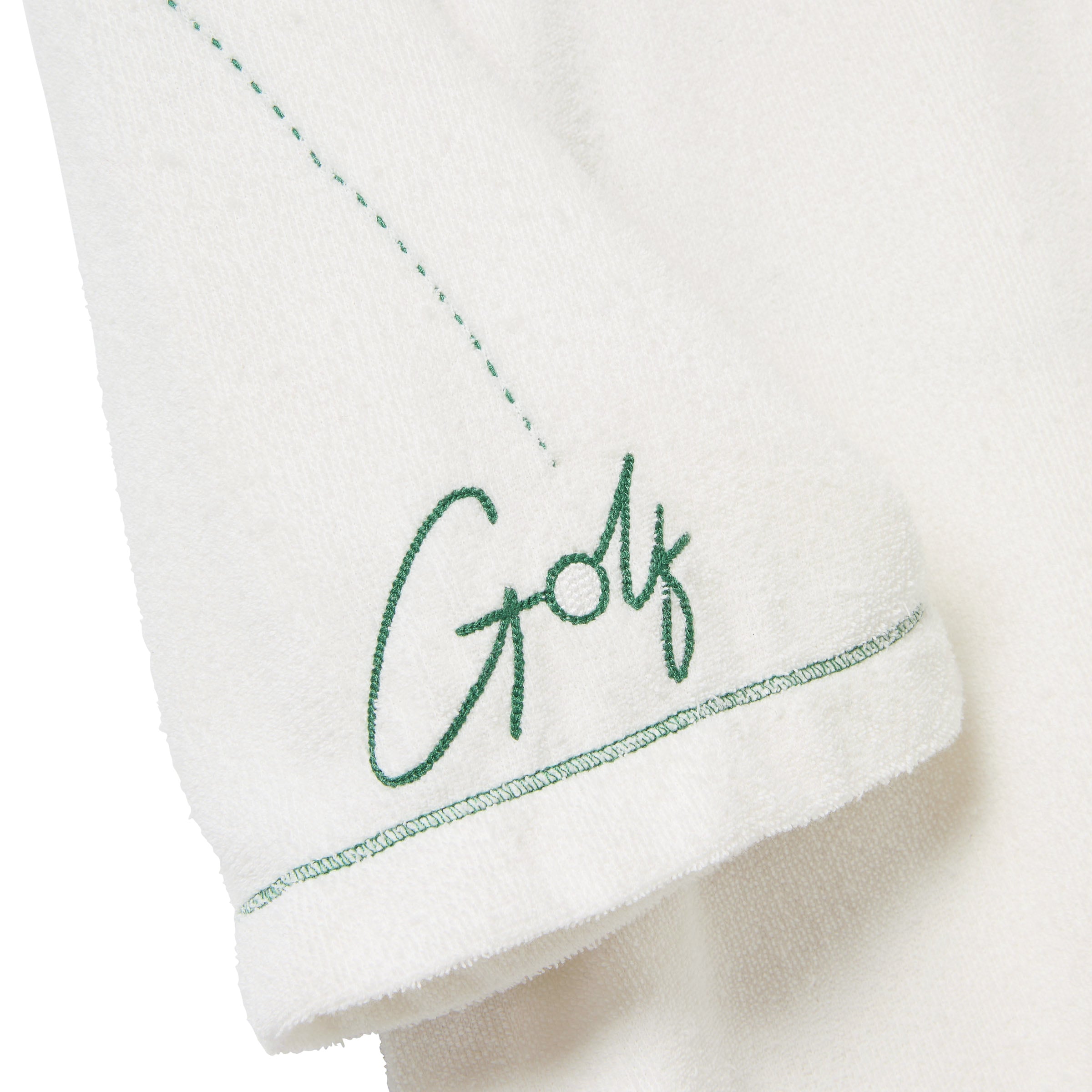 Close-up of the left sleeve of a white terry cloth polo shirt. Green embroidery reads 'Golf' in script, with a dotted line extending upward from the lettering. 