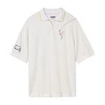 White terry cloth polo shirt with a yellow-trimmed collar. Features embroidered tennis player on the left chest and the word 'Tennis' with a small ball on the left sleeve. Dotted lines trail from the racket to the sleeve embroidery.