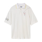 White terry cloth polo shirt with a yellow-trimmed collar. Features embroidered tennis player on the left chest and the word 'Tennis' with a small ball on the left sleeve. Dotted lines trail from the racket to the sleeve embroidery.