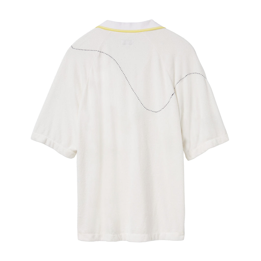 Back of a white terry cloth polo shirt with a yellow-trimmed collar. A curved black dotted line is embroidered across the upper back and shoulders, mimicking the motion of a tennis ball in play.