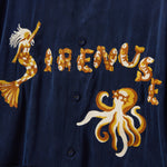 Navy blue shirt with gold mermaid, fish, and octopus embroidery on a dark background