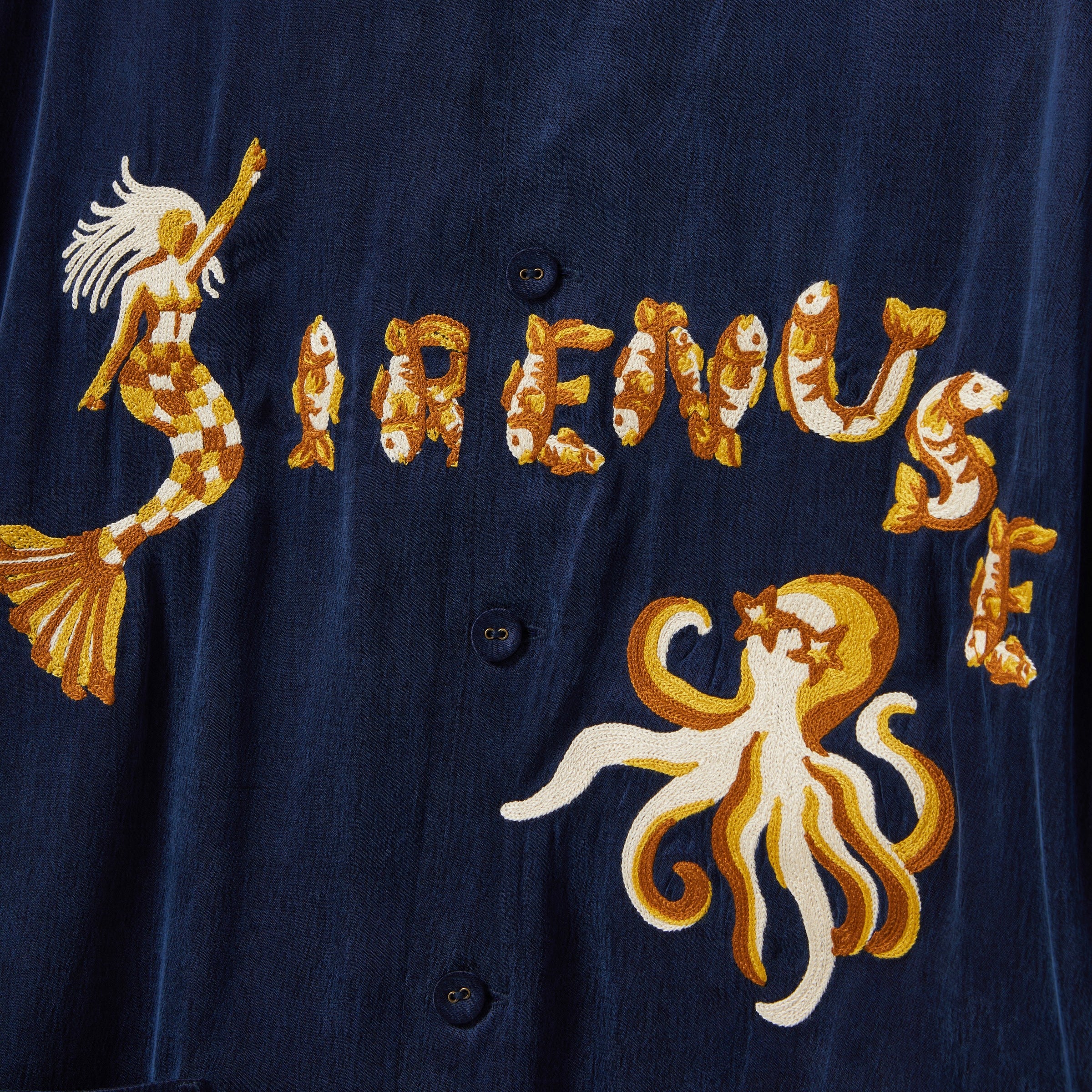 Navy blue shirt with gold mermaid, fish, and octopus embroidery on a dark background