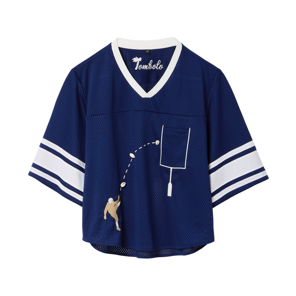 Navy blue mesh crop-cut shirt with white stripes on the sleeves, a white V-neck, and an embroidered football design showing a player kicking a football toward a goalpost outlined around the chest pocket.