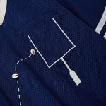 Close-up of a navy blue mesh shirt with a white outlined pocket and cowrie shells arranged to mimic a football in the air.