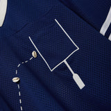 Close-up of a navy blue mesh shirt with a white outlined pocket and cowrie shells arranged to mimic a football in the air.