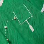 Close-up of a green mesh shirt with a white outlined pocket and cowrie shells arranged to mimic a football graphic.