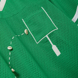 Close-up of a green mesh shirt with a white outlined pocket and cowrie shells arranged to mimic a football graphic.