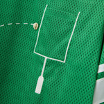 Close-up of a green mesh shirt with a white outlined pocket and cowrie shells arranged to mimic a football graphic.