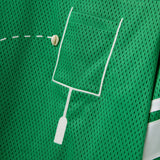 Close-up of a green mesh shirt with a white outlined pocket and cowrie shells arranged to mimic a football graphic.