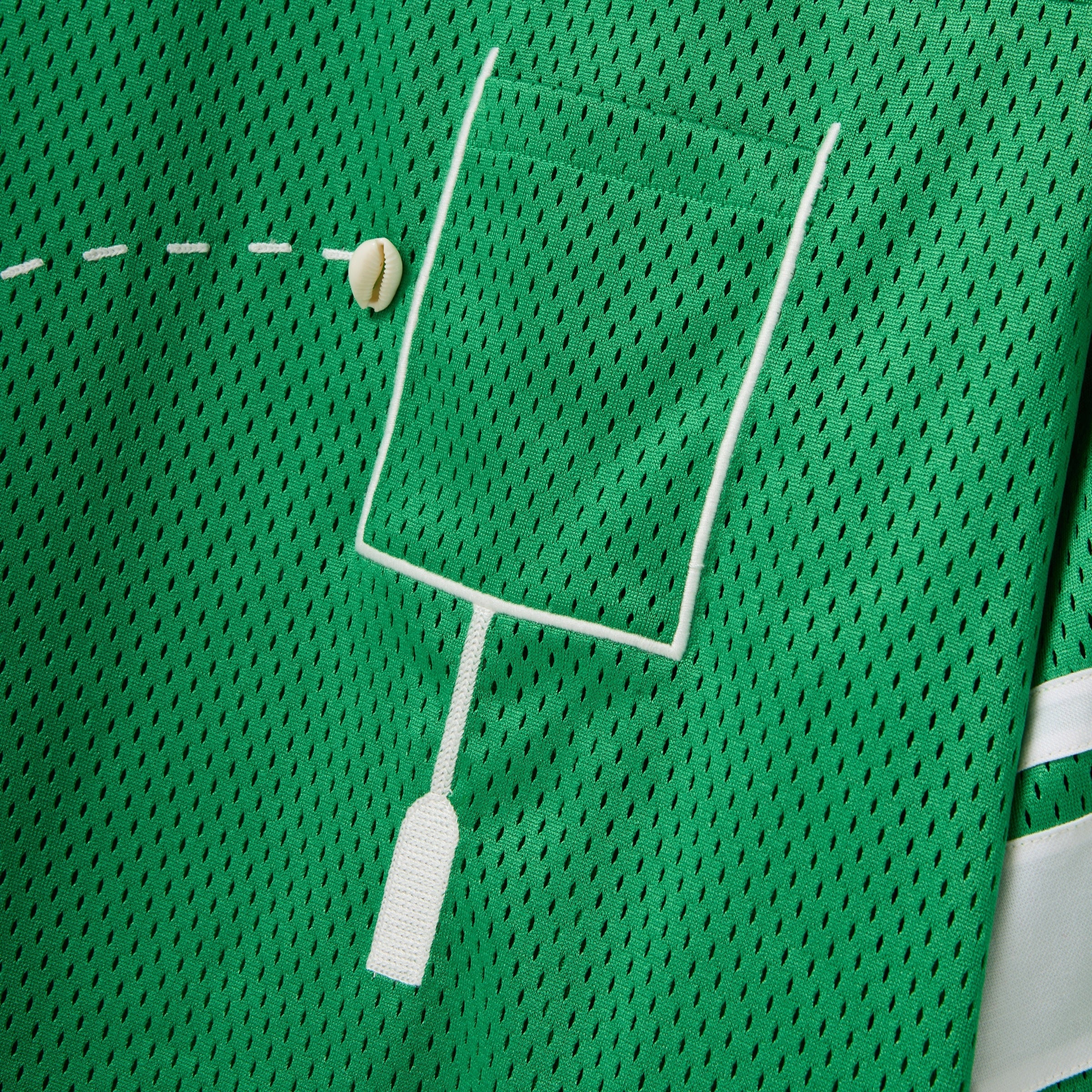 Close-up of a green mesh shirt with a white outlined pocket and cowrie shells arranged to mimic a football graphic.