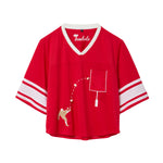 Red mesh crop-cut shirt with white stripes on the sleeves, a white V-neck, and an embroidered football design showing a player kicking a football toward a goalpost outlined around the chest pocket.